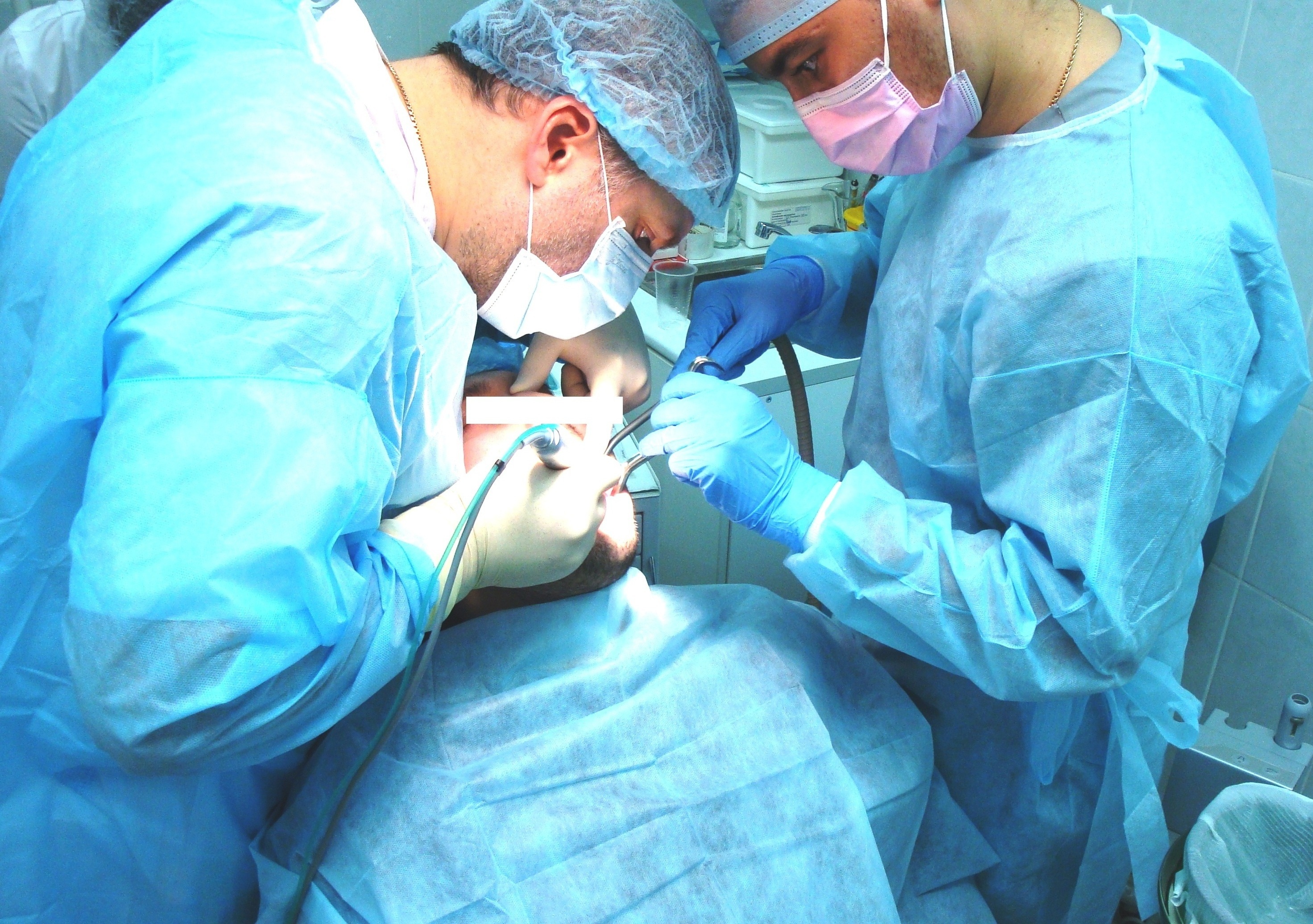 Врач-Имплантолог с ассистентом во время имплантации: пациенту М ввинчивают имплант